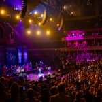 Audience watch purple lit stage with singers and band on