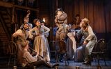 Calamity Jane (Carrie Hope Fletcher) stands on a chair, pointing a rifle as ensemble and musicians gather around, watching rapt