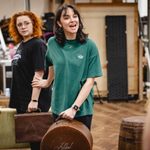 Seren Sandham-Davies (Katie Brown) gently holds Carrie Hope Fletcher (Calamity Jane) behind her as she talks to a shoulder just in shot, both hold old luggage