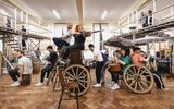 Wagon wheels by the side of the piano and chairs form an imagined carriage, with Carrie Hope Fletcher (Calamity Jane) sitting up top with the driver, shooting an umbrella like a riffle, in the back people crowd under umbrellas