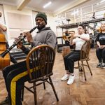 Carrie Hope Fletcher (Calamity Jane) sits primly sideways on a chair, musicians sitting similarly in a row of chairs