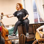 Carrie Hope Fletcher (Calamity Jane) sings, telling a tale as she sits on top of a piano, Jacob Leeson (Swing) with a double bass and Molly-Grace Cutler (Adelaide Adams) with a guitar looking up at her in concern