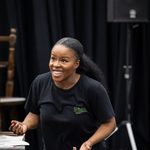 Leah Hill (choreographer) leans forward slightly as though intently engaged with someone off camera, hands mid gesture, wearing black wicked t-shirt