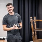 Liam Doyle grins, holding a camera next to an upturned stool