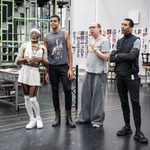 Newtion Matthews in white crop top, skirt, knee high socks attached to suspenders and headband standing next to Kofi Dennis, Jonathan Dryden Taylor & Ashley-Jordon Packer