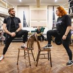 Vinny Coyle (Wild Bill Hickok) and Carrie Hope Fletcher (Calamity Jane) mirroring each other with one leg up on back to back chairs, glaring at each other