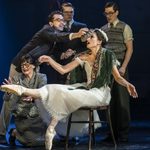 Irina Boronskaja (Michela Meazza) sit on a chair, shawl over shoulders, leg outstretched. A woman cups her hands around her foot but doesn't touch, a smoking man pressed a cold compress to Irina's head and two others stand behind looking concerned.