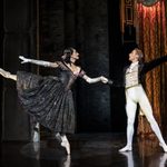 Irina Boronskaja (Michela Meazza, wearing black sparkly dress and white gloves) and Ivan Boleslawsky (Liam Mower, wearing black jacket, white trousers and waistcoat) dance together, hands clasped as Irina stands on one leg, both free hands thrown behind them