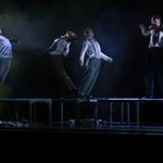 Three Dancers stand curved backwards on platforms as a forth raises his fists head level