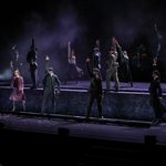 The Rambert Dancers stand at different levels, one hand thrown in the air.