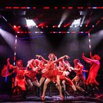 Lola (Johannes Radebe) in sparkly red small dress and short red wig with backing dancers