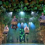 Four school kids lie on their stomachs on swings, swinging high is an arch of wooden scrabble-like tiles