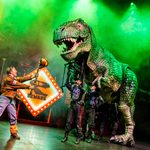 Large T-rex puppet looms out of the haze towards ranger holding up ball on stick