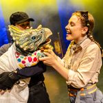 Puppeteer holds a baby triceratops puppet wrapped in blankets as white brunette ranger coos over it