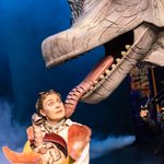 Female ranger, looking concerned, holding baby Giraffatitan in egg as big Giraffatitan puppet licks her cheek