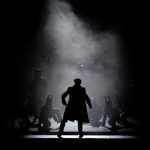 202503PeakyBlinders@BeatriceLivet-13 Silhouette of man in coat and peak cap facing dancers in dog hats and their handlers