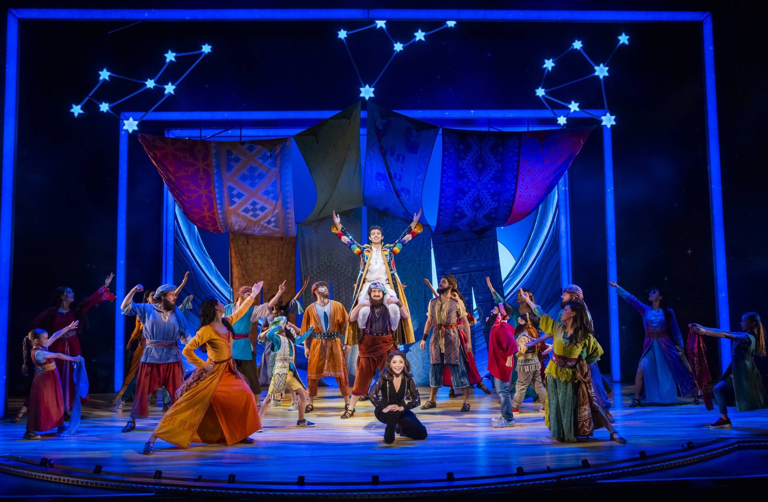Joseph and the Amazing Technicolor Dreamcoat Joseph (Adam Filipe) in the technicolor coat, sitting on the shoulders on one of his brothers as the others and ensemble point up at him, the Narrator (Christina Bianco) kneels in front.