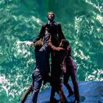 Four men in suits lifting up man in front of sea background