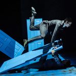 Man lying on floor holding up blue door. Second man leaning on door.