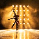 Man stood on right leg doing dramatic ballet pose with gold background.