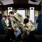 Group of men in train carriage looking left.