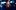 Christina Bianco - The Narrator Woman in black extends arms to audience, standing in front of stage lights