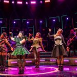Six women in glittery costumes pointing to the right. Credit Pamela Raith.
