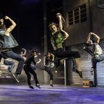 Several ensemble dance members mid-leap during a dance number