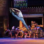 Image of a man in a white t-shirt and blue jeans leaping and doing a high kick